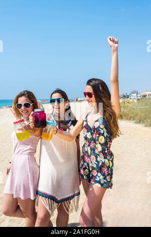 friendship and leisure concept - group of happy young women or female friends toasting non alcoholic drinks on summer beach Stock Photo