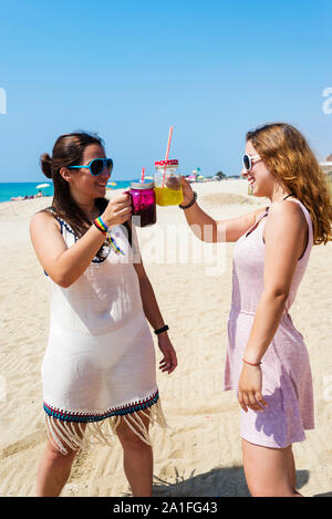 friendship and leisure concept - group of happy young women or female friends toasting non alcoholic drinks on summer beach Stock Photo