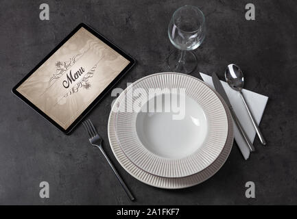 Tablet with stylish restaurant logo and laid table Stock Photo