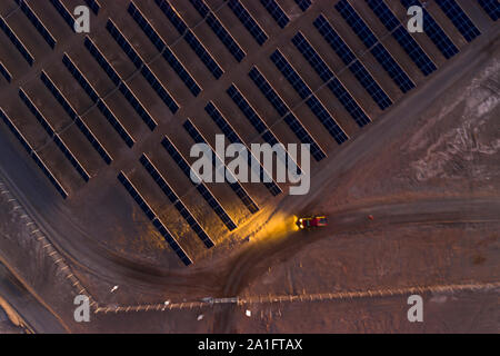 Pick up truck with the lights on and it workers finishing the day prepared for going home. A view of a remote Solar Energy farm with it solar modules Stock Photo
