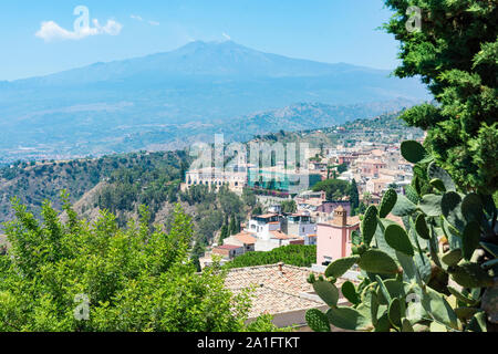 Beautiful view to Taormina city, Sicily, Italy and Etna volcano. Old houses and green plants. Smoke coming out of the crater of the volcano.