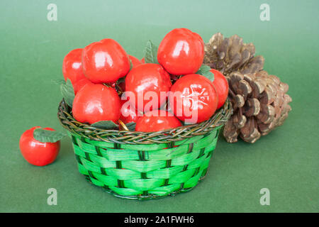 Decorative red apples in a basket and cones on a green background. Stock Photo