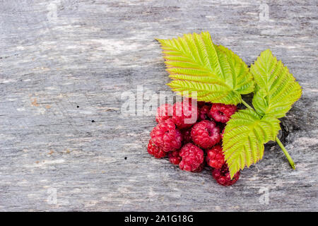 juicy raspberries lying on an old wooden table with three green leaves Stock Photo