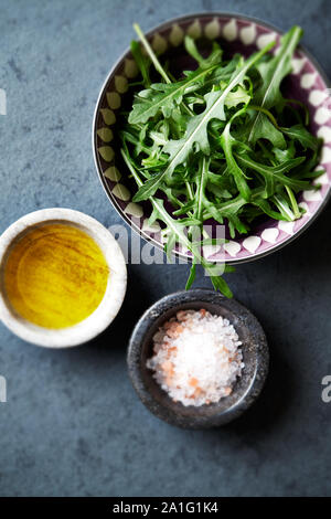 Fresh arugula, flax oil and himalayan salt for salad in small ceramic bowls on dark stone background. Stock Photo