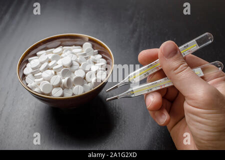 man is going to eat the drug tablets in bowl and holds two medical thermometer like chopsticks Stock Photo