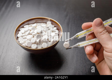 man is going to eat the drug tablets in bowl and holds two medical thermometer like chopsticks Stock Photo