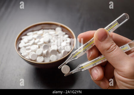 man is going to eat the drug tablets in bowl and holds two medical thermometer like chopsticks Stock Photo