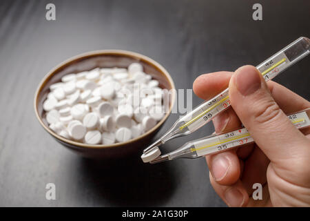 man is going to eat the drug tablets in bowl and holds two medical thermometer like chopsticks Stock Photo