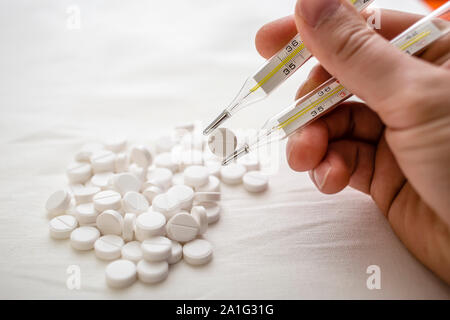 man is going to eat the drug tablets and holds two medical thermometer like chopsticks Stock Photo