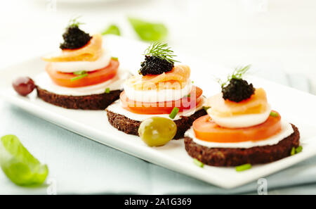 Canapes with smoked salmon, soft cheese, eggs, tomato, caviar and fresh basil. Symbolic image. Concept for a tasty and healthy meal Stock Photo