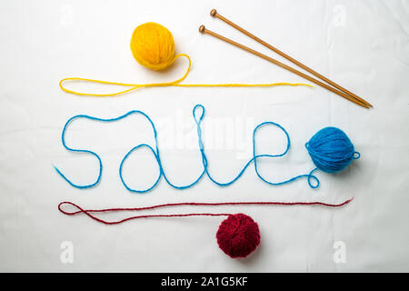 Word sale written multicolored yarn threads coiled into balls on a white background, near wooden spokes lie Stock Photo