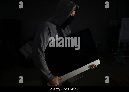 Thief in balaclava carries PC from apartment of victims Stock Photo