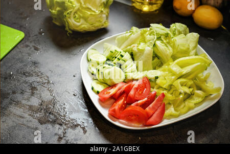 Cut tomatoes, cucumber and iceberg salad on dark kitchen board Stock Photo