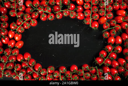 Top down view, heap of cherry tomatoes with green vine leaves arranged in circle frame on black marble like board, space for text at middle Stock Photo