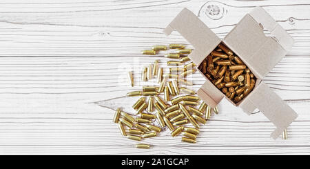 Top down view, carton box with yellow brass ammunition bullets on white wooden desk, banner - space for text left side Stock Photo