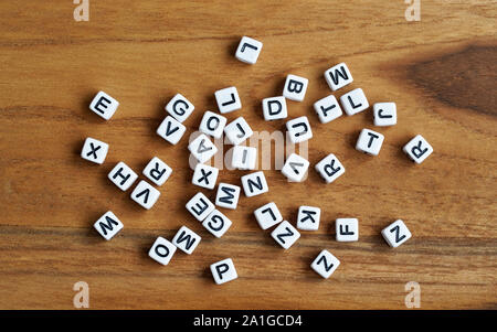 Small white cube beads with various letters scattered on wooden board, view from above Stock Photo