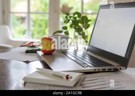 home office workspace for a small business, on the desk a laptop with empty screen, papers, coffee cup, glasses and a bitten apple, selected focus, na Stock Photo