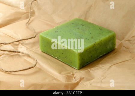 Green handmade herbal soap bar on a brown wrapping paper. Natural toiletries and hygiene products with herbs and essential oils. Front view. Stock Photo