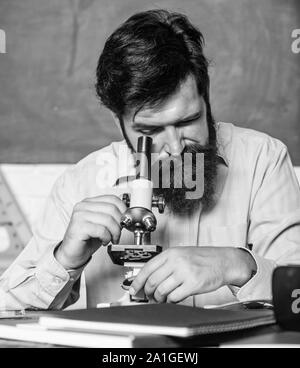 Set up microscope. Teacher sit desk with microscope. Man bearded hipster classroom chalkboard background busy with biological observation. School teacher looking microscope. Fascinating research. Stock Photo