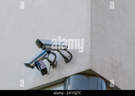 Two Security Cameras set up on the exterior dirty white rough concrete wall at corner of building. Stock Photo