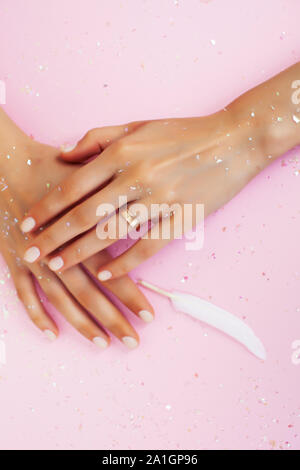 beautiful manicured woman hands with white feather on pink background, wearing wedding ring