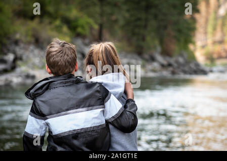 The close up of the backs of the teenage girl and boy hugging outside in the nature. Stock Photo