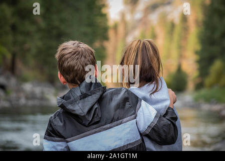 The close up of the backs of the teenage girl and boy hugging outside in the nature. Stock Photo