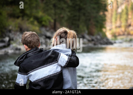 The close up of the backs of the teenage girl and boy hugging outside in the nature. Stock Photo