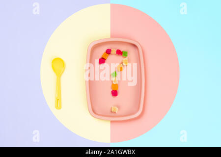 Minimalistic flat bark with a plastic pink plate on which is a question mark of candied pineapple and a yellow spoon in a yellow-pink isolated backgro Stock Photo