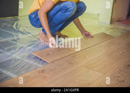 Man installing new wooden laminate flooring on a warm film floor. infrared floor heating system under laminate floor Stock Photo