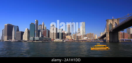 Lower Manhattan skyline, Eastern River and Brooklyn Bridge with a yellow water taxi boat on the foreground, New York City Stock Photo