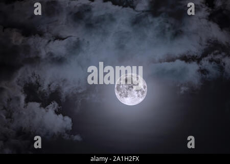 Night sky and a full moon in the clouds. Full moon against the dark night sky. Stock Photo