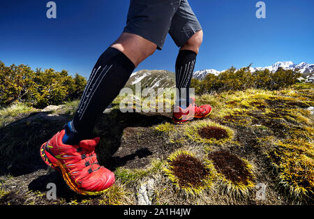 Close up of hiker legs in red shoes are climbing in the mountains at blue sky background. Healthy lifestyle. Outdoor travel concept. Stock Photo