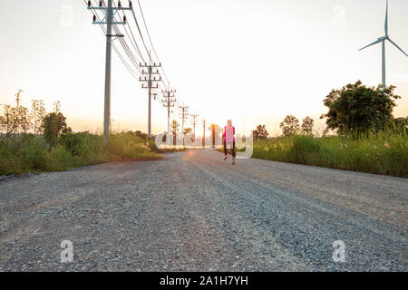 The evening sunset, The area of the wind turbine generates clean energy electricity, A woman is jogging on the road. Stock Photo