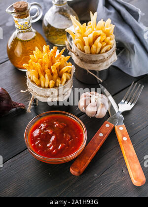 French fries in a metal mug with tomato sauce on a rustic background. Portion potato fries. Tasty Snack from fast food. Fork, spoon, napkin. Vertical Stock Photo