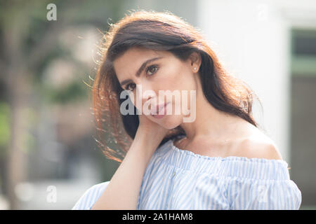 Shy but flirty brunette tucking her hair behind her ear, closeup, sunny warm day Stock Photo