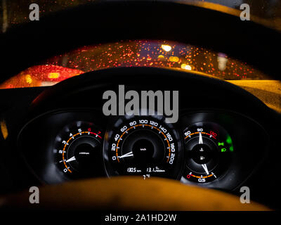 Glowing car dashboard at night against the background of raindrops on the windshield in the reflection of street lights. Abstract image of city life. Stock Photo