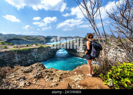 Travel people with backpack and in shorts on the ocean, cliffs and tropical beach background. Angel's Billabong beach, Nusa Penida, Indonesia. Stock Photo