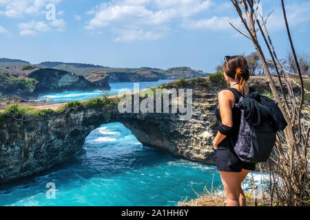 Travel people with backpack and in shorts on the ocean, cliffs and tropical beach background. Angel's Billabong beach, Nusa Penida, Indonesia. Stock Photo