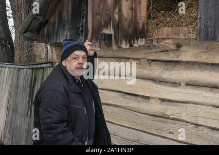 Outdoor portrait of Ukrainian old man standing near his barn with hay and looking with hope Stock Photo