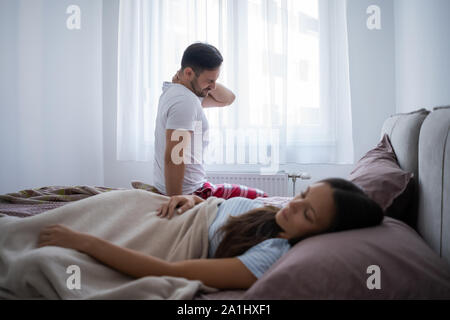 Young couple is waking up in the morning. Man has pain in neck. Stock Photo