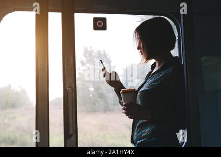 Pretty woman with a phone and a cup of coffee is standing in the train Stock Photo