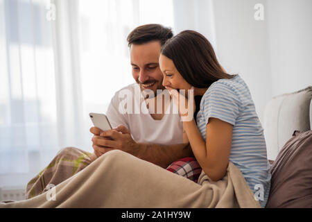 Young happy couple is looking at smartphone in bed in the morning. Stock Photo