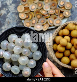 Top view Vietnamese tropical sweet, watery pulp fruit, close up Longan fruits flesh in translucent white on black plate with black seed, yellow peel, Stock Photo