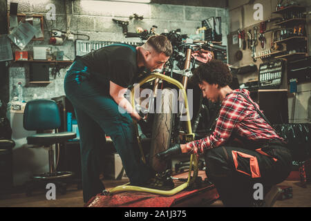 Mechanic and his helper repairing a motorcycle in a workshop Stock Photo