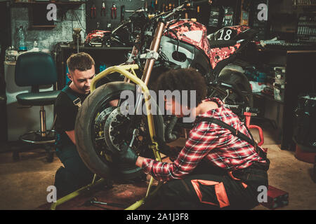Mechanic and his helper repairing a motorcycle in a workshop Stock Photo