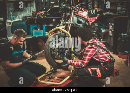 Mechanic and his helper repairing a motorcycle in a workshop Stock Photo