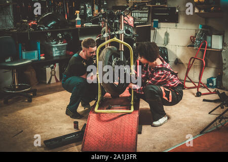 Mechanic and his helper repairing a motorcycle in a workshop Stock Photo