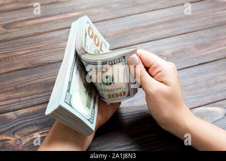 Perspective view of a businesswoman's hands counting one hundred dollar banknotes on wooden background. Success and wealth concept. Stock Photo