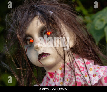 Disgarded demon doll with red eyes lies hidden in bushes Stock Photo